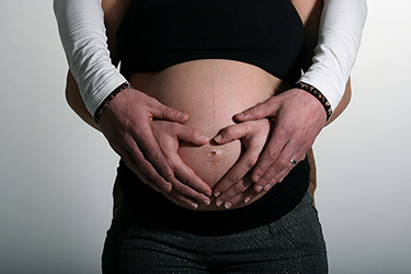 grossesse heureuse photographiée par notre photographe Rachel Joubi, mains du couple placés en forme de coeur sur le ventre de la futur maman